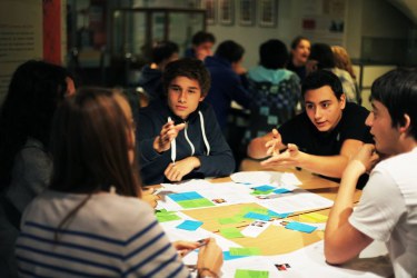 A group of students pictured around a table while playing a PlayDecide game