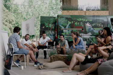 In this picture background is the Climate Capsule (Klimatska Kapsula) - a van created by artists who's graphics echoe nature & climate crisis. At the front is the public having a discussion