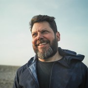 Image of white middle aged man outdoors with sky background. 