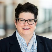 woman wearing glasses and dark blue blazer, she is smiling 