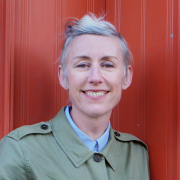 A picture of Dee Halligan smiling female against a red background 