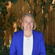 A photo of a blond woman in a blue jacket in front of a wood fence