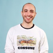 Khalil sitting and smiling, wearing a white t shirt with a caterpillar and the word CONSUME on the front
