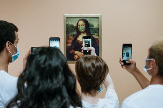 People taking a picture of the Mona Lisa wearing a face mask. 